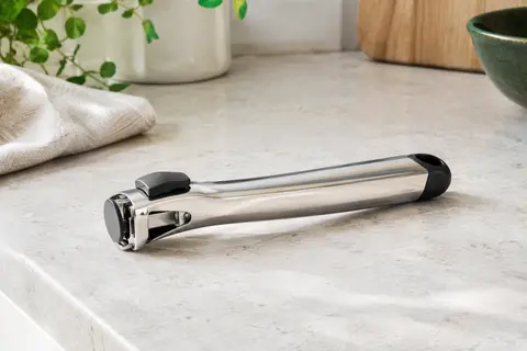Poignée amovible Cristel en inox brillant avec bouton noir, posée sur un plan de travail clair