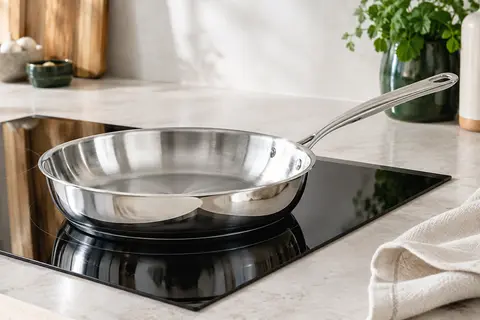 Poêle à frire De Buyer Milady en inox poli brillant avec poignée rivetée, posée sur une plaque à induction.