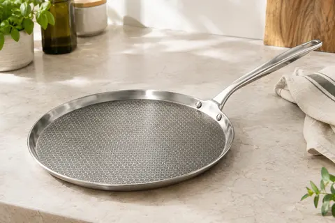 Poêle à crêpes Innerwell en inox avec surface alvéolée et longue poignée, posée sur un plan de travail clair.